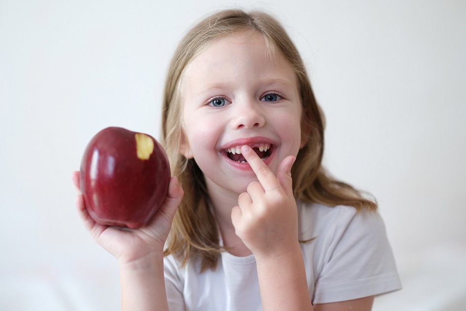 Smiling Girl Without Tooth Is Holding Apple. Pediatric Dentistry Emerald Dental - pediatric emergency